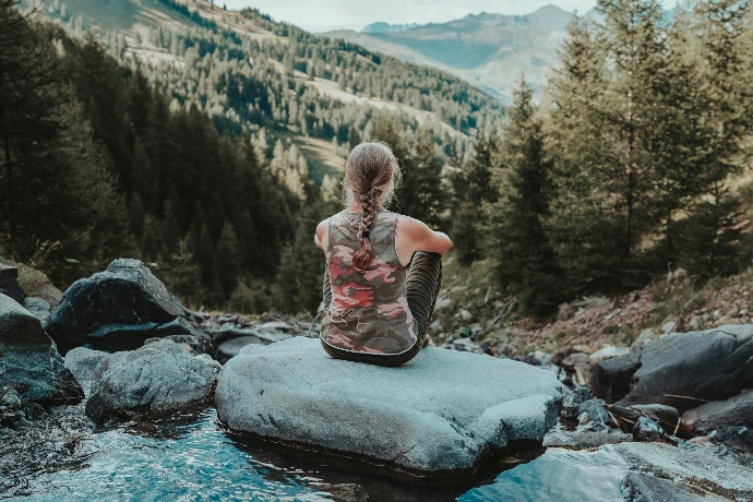 a woman sitting on a rock in the middle of a stream